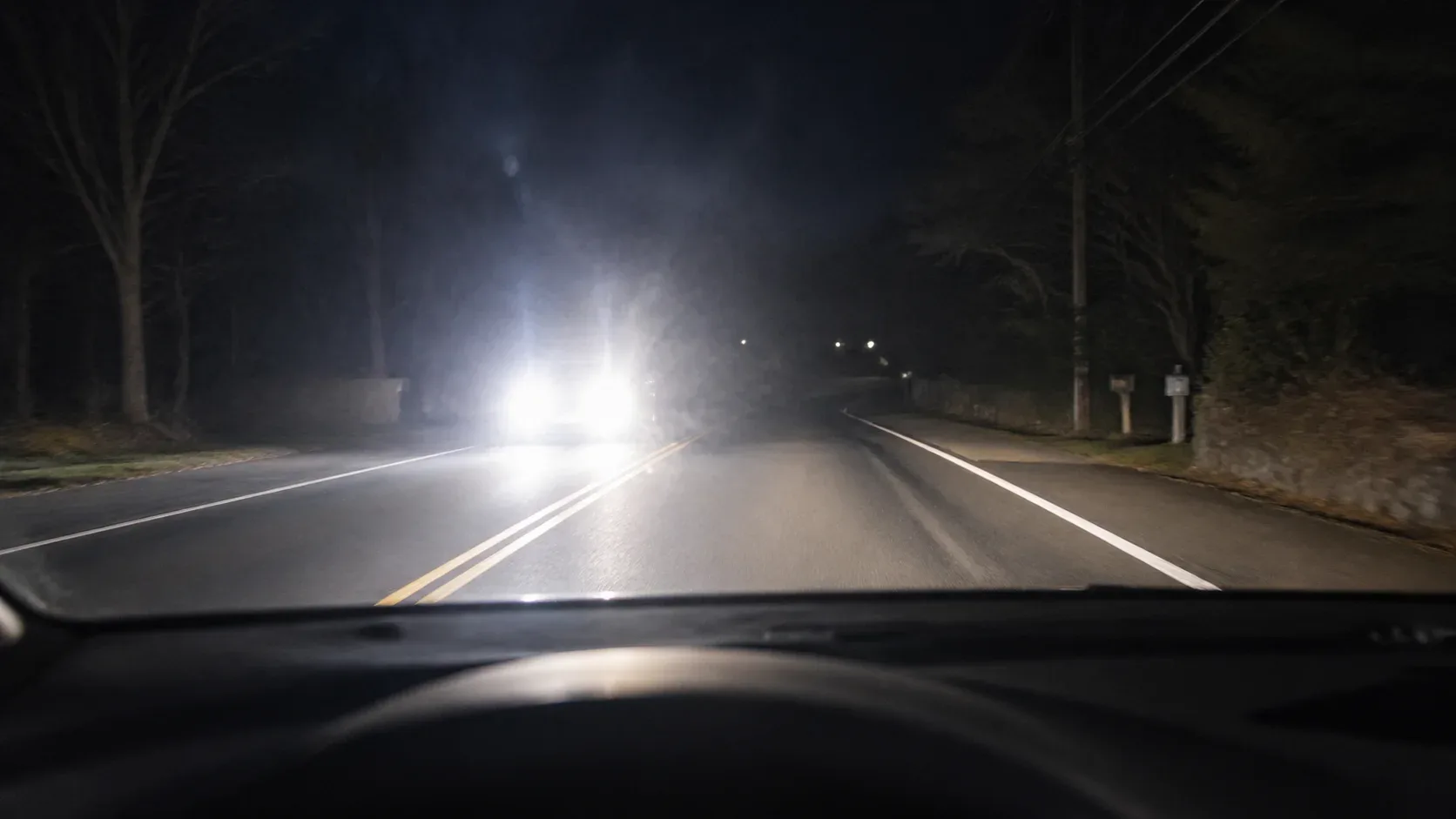 Night driving view with harsh oncoming high beams blooming through the windshield.